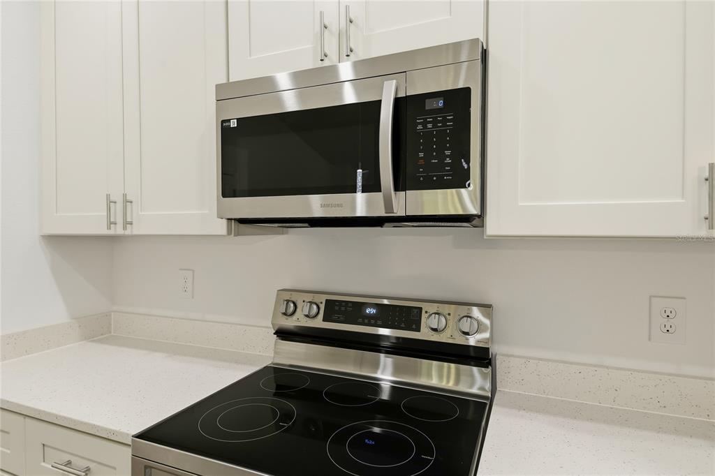 A stainless steel microwave and electric range are installed between white cabinets and countertops — 224 GLADIOLA COURT, POINCIANA, FL