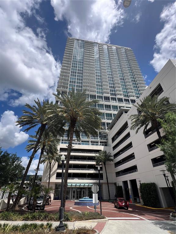 A tall residential high-rise building with an attached parking garage and palm trees in front — 150 E ROBINSON STREET UNIT 2409, ORLANDO, FL