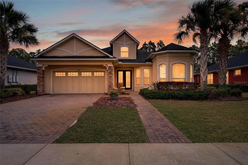 A single-story house with a two-car garage, brick walkway, and palm trees at sunset — 349 CHELSEA PLACE AVENUE, ORMOND BEACH, FL