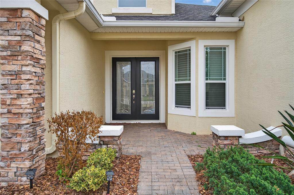 A stone-accented entryway features a paved walkway leading to double glass-paneled front doors — 349 CHELSEA PLACE AVENUE, ORMOND BEACH, FL