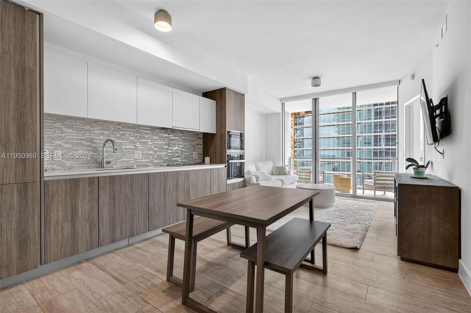 A modern kitchen and living area feature wood-toned cabinetry, a dining bench, and floor-to-ceiling windows — 2900 NE 7th Ave # 1108, Miami FL 33137, MIAMI, FL