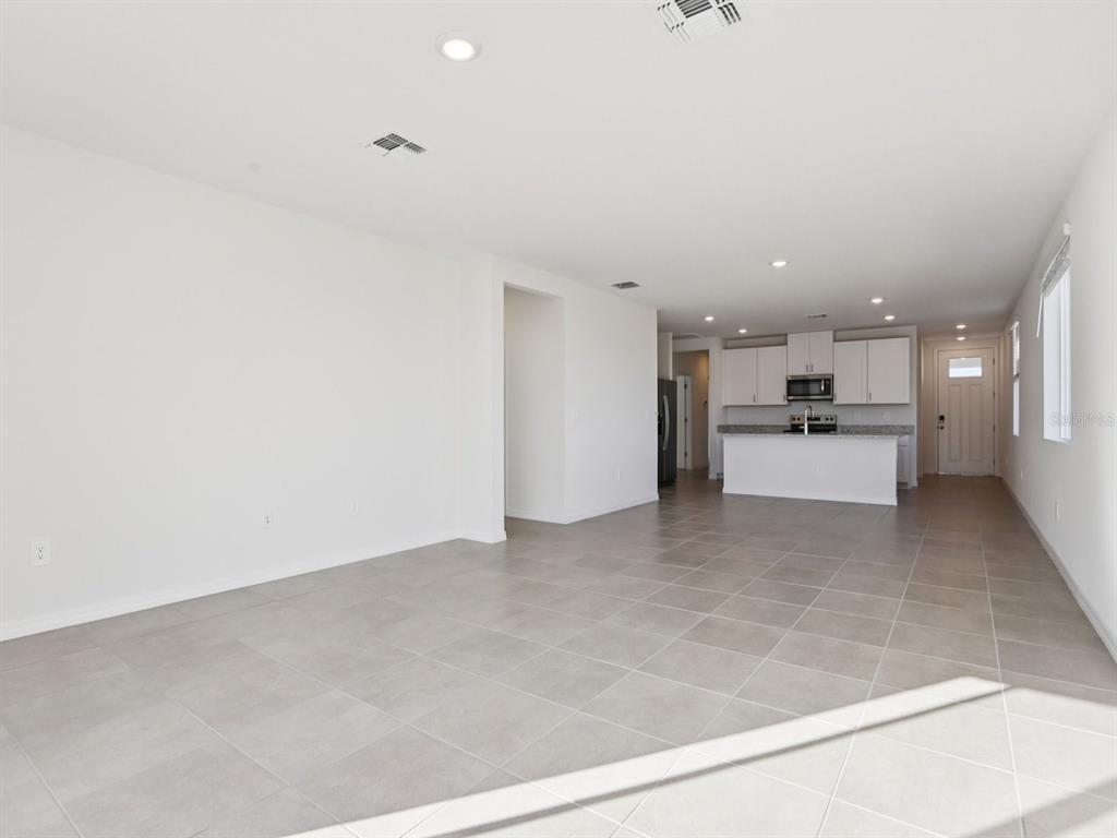 An open-concept living area with light tile flooring leads to a kitchen with white cabinets — 11337 BELLEWOOD TERRACE, PARRISH, FL