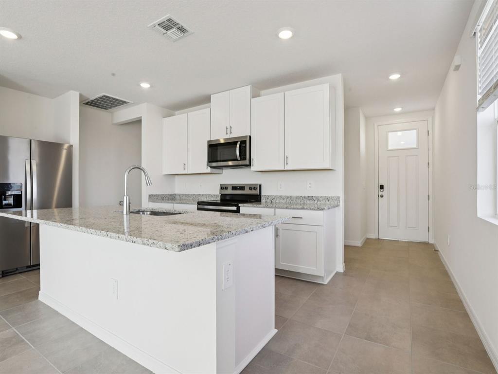 A kitchen features white cabinets, granite countertops, a center island, and stainless steel appliances — 11337 BELLEWOOD TERRACE, PARRISH, FL