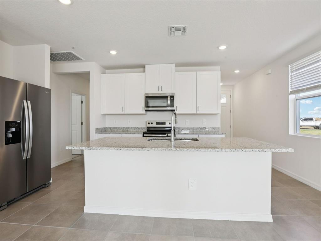 A modern kitchen features white cabinets, granite countertops, a central island, and stainless steel appliances — 11337 BELLEWOOD TERRACE, PARRISH, FL
