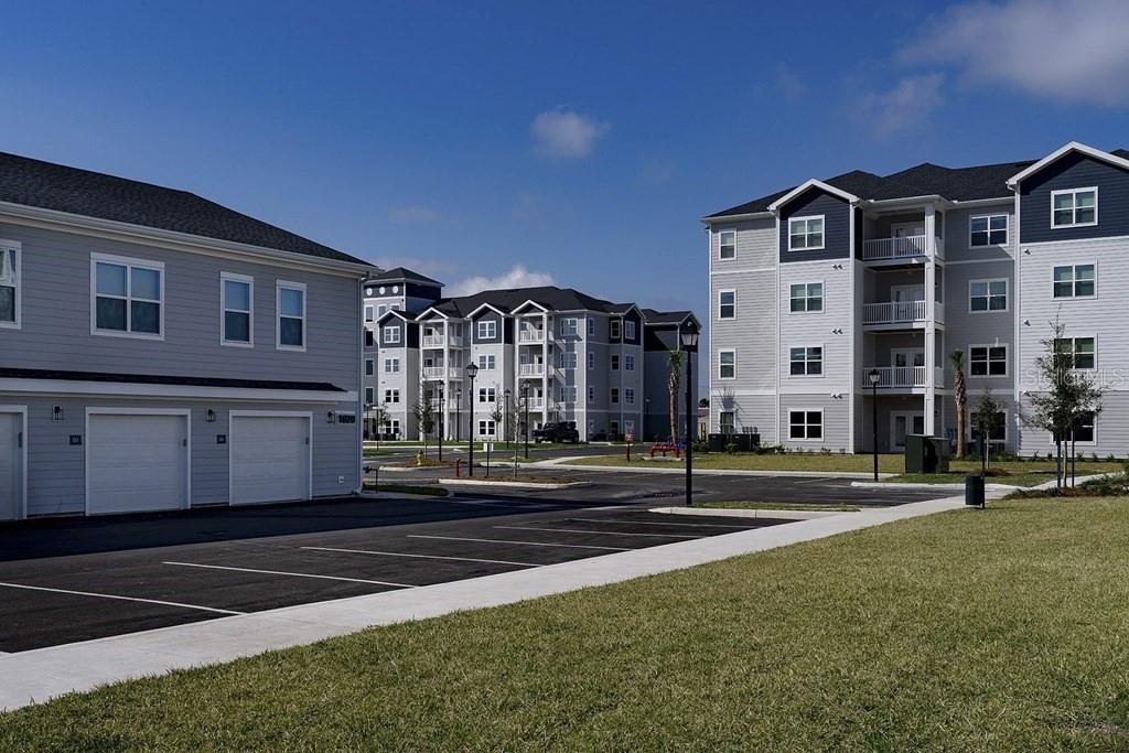 Exterior view of multi-story apartment buildings with gray siding, attached garages, and a parking lot — 1015 LAKE FOREST BOULEVARD UNIT A2, WINTER HAVEN, FL