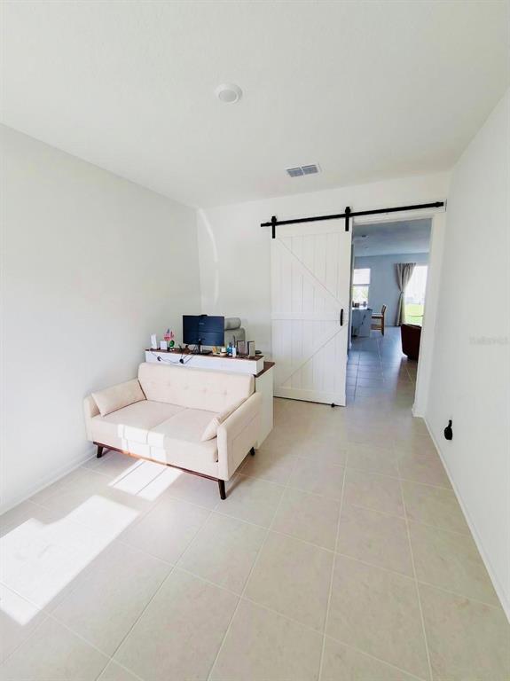 A small room features a beige loveseat, a desk with a monitor, and a sliding barn door — 3035 MINDFULLNESS DRIVE, CLERMONT, FL