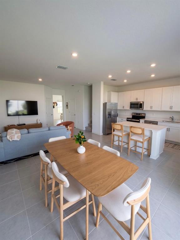 An open-concept living area features a dining table, kitchen island with stools, and a sofa — 3035 MINDFULLNESS DRIVE, CLERMONT, FL