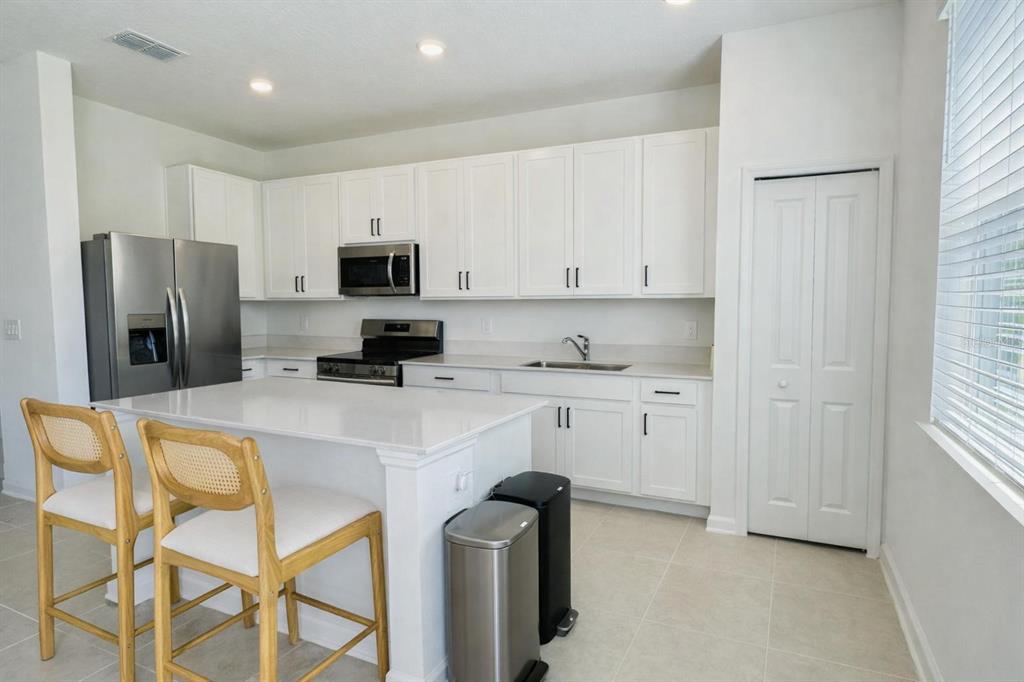A modern kitchen features white cabinets, stainless steel appliances, a quartz island, and two chairs — 3035 MINDFULLNESS DRIVE, CLERMONT, FL
