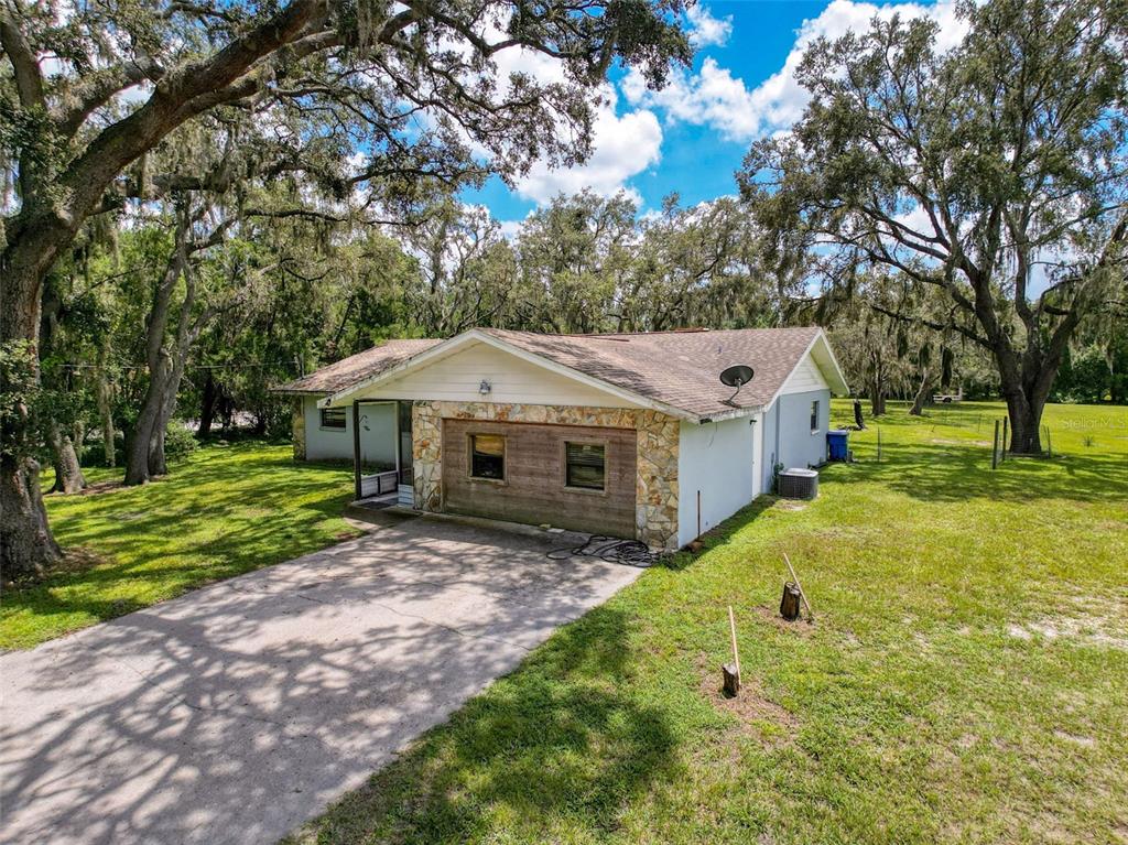 A single-story house with a stone-accented facade, a concrete driveway, and large surrounding oak trees — 15438/15440 AZRA DR, ODESSA, FL