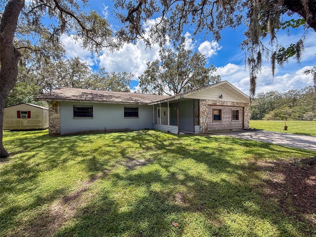 A single-story house with stone accents, a covered porch, and a detached shed on grass — 15438/15440 AZRA DR, ODESSA, FL