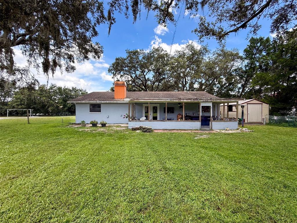 A single-story house with a screened-in porch, a bright orange chimney, and a detached shed — 15438/15440 AZRA DR, ODESSA, FL