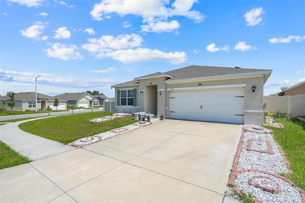 A single-story house with a two-car garage, light-colored stucco exterior, and decorative rock landscaping — 1105 TORRENTE LANE, HAINES CITY, FL