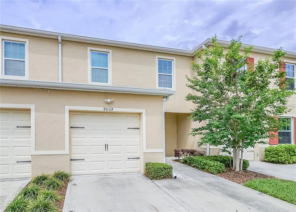 A two-story tan stucco townhouse with a single-car garage and a small front tree — 9039 ALBA LANE, KISSIMMEE, FL