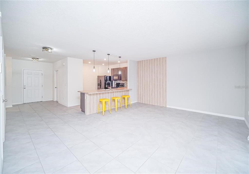 An open-concept living area features light gray tile flooring, a kitchen island, and yellow stools — 9039 ALBA LANE, KISSIMMEE, FL