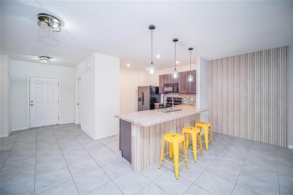 A kitchen features a slatted wood island with yellow stools, tile flooring, and dark cabinetry — 9039 ALBA LANE, KISSIMMEE, FL