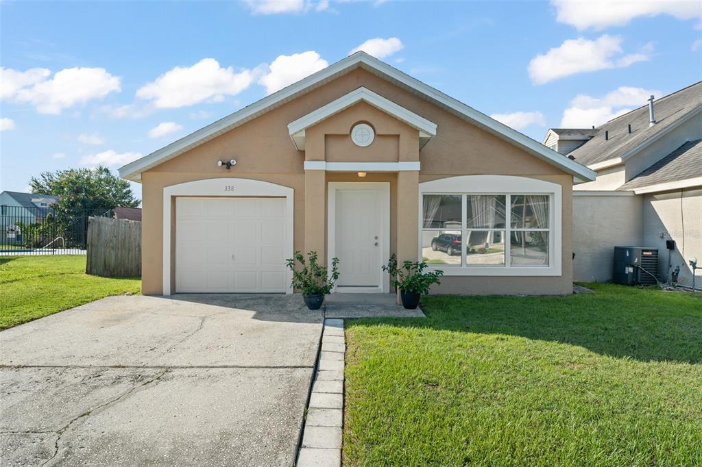 A single-story house with a tan stucco exterior, a one-car garage, and a front lawn — 338 WINDFORD COURT, WINTER GARDEN, FL