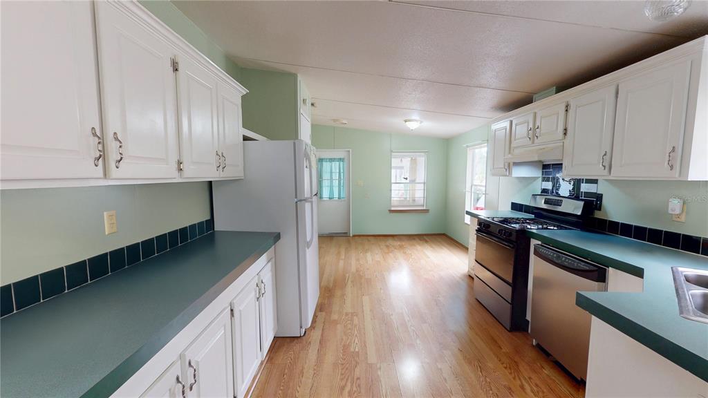 A kitchen features white cabinets, green countertops, a stainless steel stove, and light wood flooring — 2031 PORTO BOULEVARD, NEW SMYRNA BEACH, FL