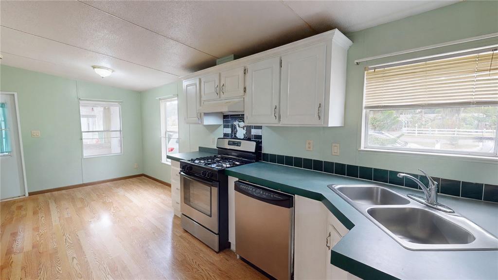 A kitchen features white cabinets, green countertops, stainless steel appliances, and light wood flooring — 2031 PORTO BOULEVARD, NEW SMYRNA BEACH, FL