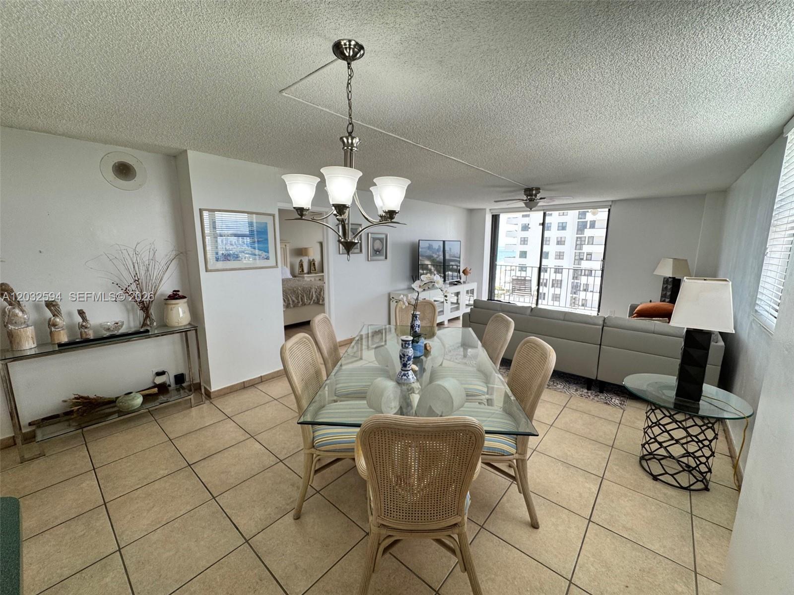 A dining area with a glass table and wicker chairs sits before a living room — 2625 Collins Ave # 1801, Miami Beach FL 33140, MIAMI BEACH, FL