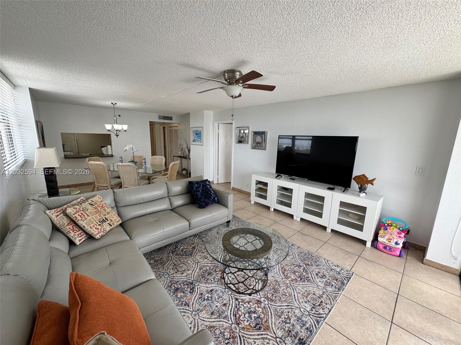 A living room features a grey sectional sofa, a glass coffee table, and a television console — 2625 Collins Ave # 1801, Miami Beach FL 33140, MIAMI BEACH, FL