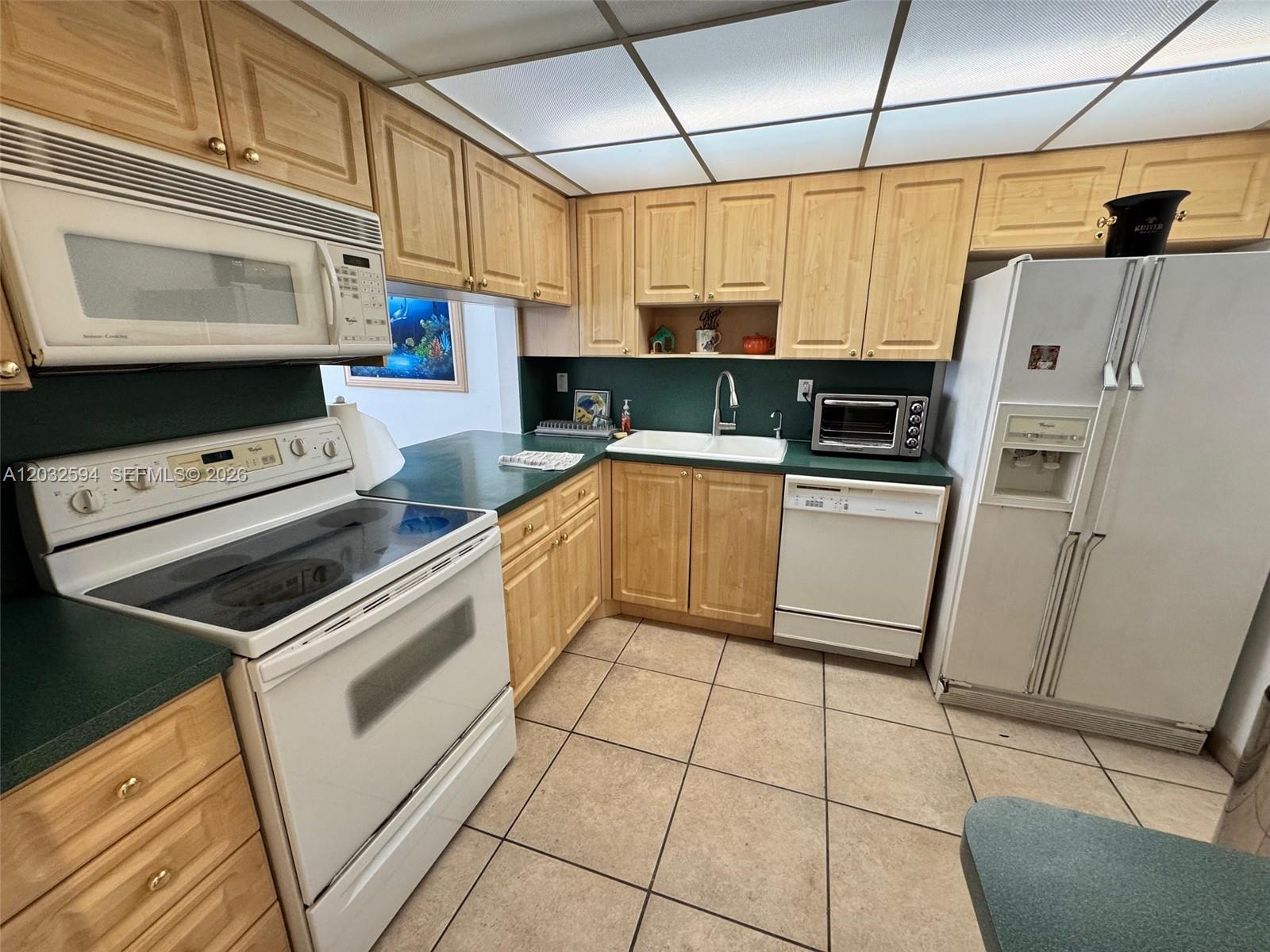 A kitchen features light wood cabinets, green countertops, white appliances, and a tiled floor — 2625 Collins Ave # 1801, Miami Beach FL 33140, MIAMI BEACH, FL