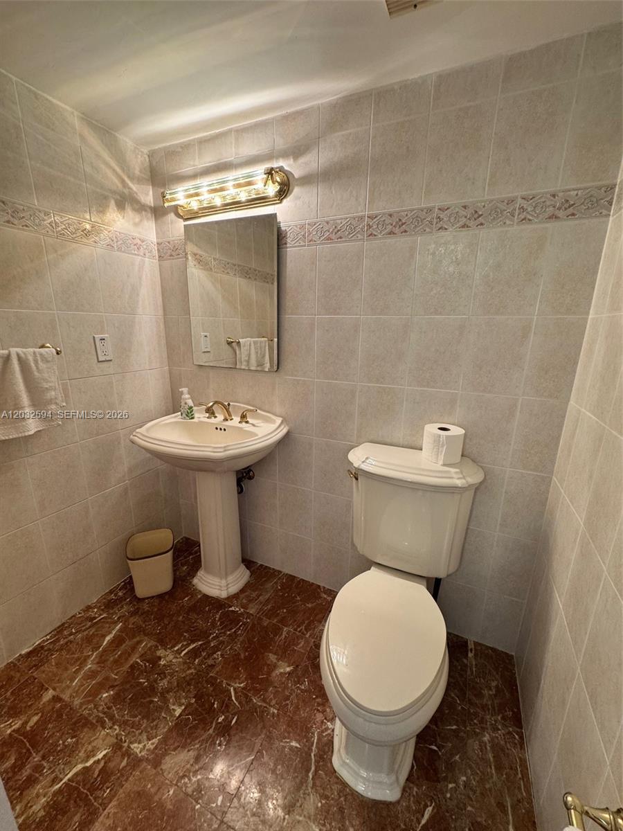 A small bathroom features a pedestal sink, a toilet, and beige tiled walls — 2625 Collins Ave # 1801, Miami Beach FL 33140, MIAMI BEACH, FL