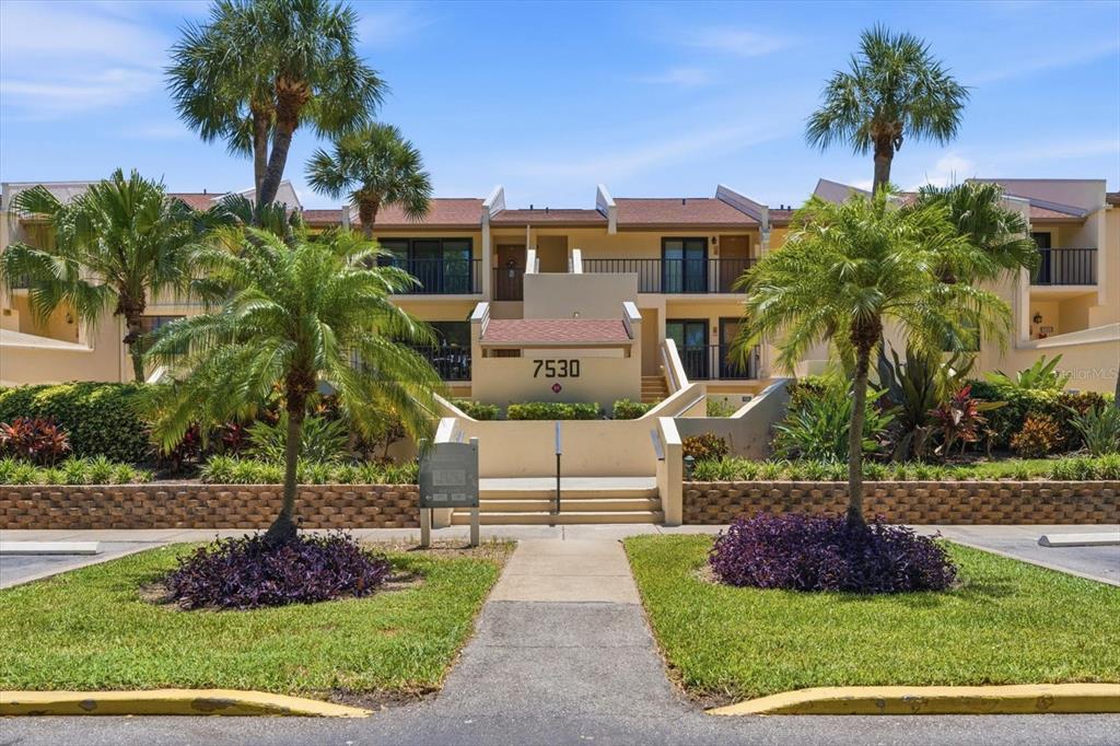 A multi-story apartment building with tan stucco walls, balconies, and palm trees in front — 7530 SUNSHINE SKYWAY LANE S UNIT T30, ST PETERSBURG, FL