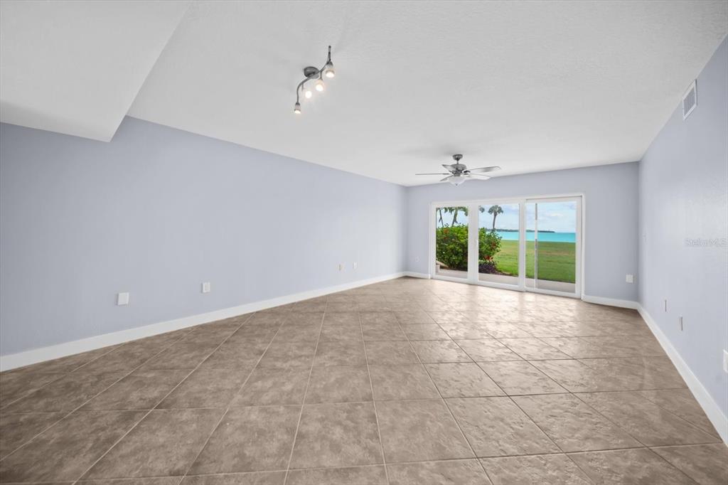 An empty room with light blue walls, tile flooring, and sliding glass doors overlooking water — 7530 SUNSHINE SKYWAY LANE S UNIT T30, ST PETERSBURG, FL