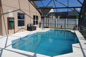 A swimming pool sits inside a screened-in lanai next to a tan house — 836 CASSIA DRIVE, DAVENPORT, FL