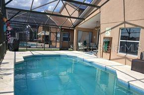A swimming pool sits inside a screened-in lanai next to a tan house — 836 CASSIA DRIVE, DAVENPORT, FL