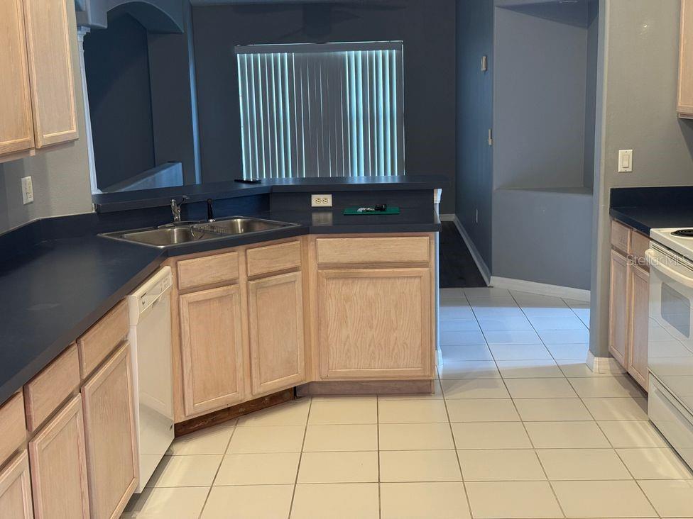 A kitchen features light wood cabinets, dark countertops, white appliances, and light-colored tile flooring — 836 CASSIA DRIVE, DAVENPORT, FL