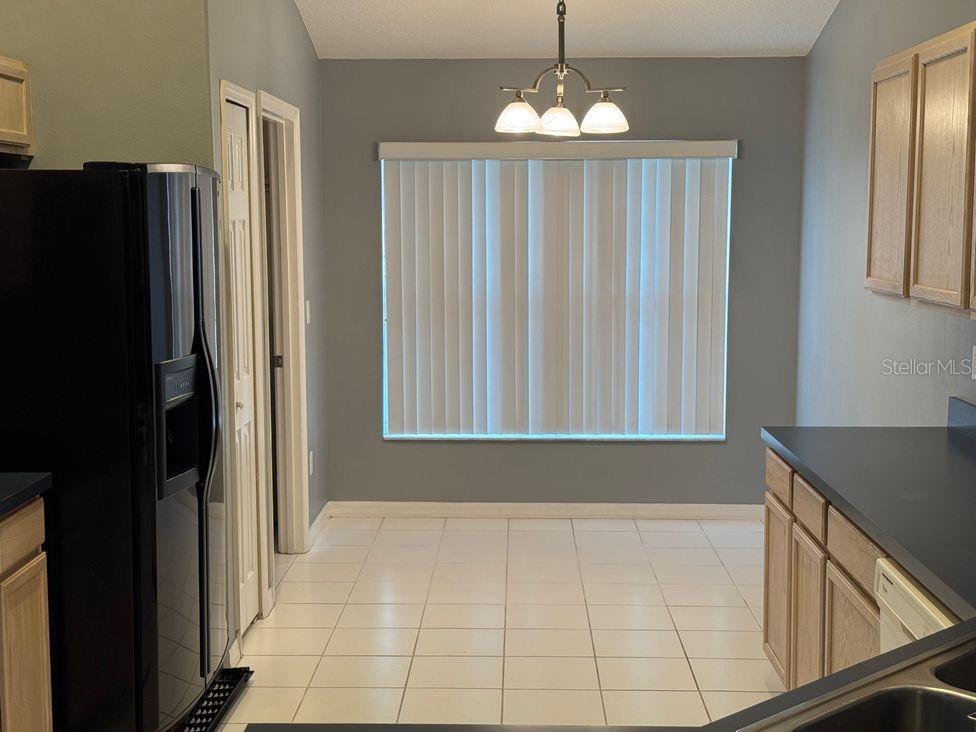 A kitchen with light wood cabinets, black appliances, tile flooring, and a window with blinds — 836 CASSIA DRIVE, DAVENPORT, FL