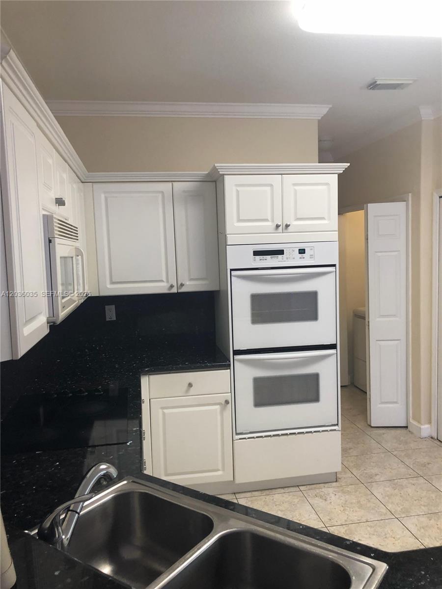 A kitchen features white cabinets, black countertops, and a double wall oven — 11253 NW 47th Ln, Doral FL 33178, DORAL, FL