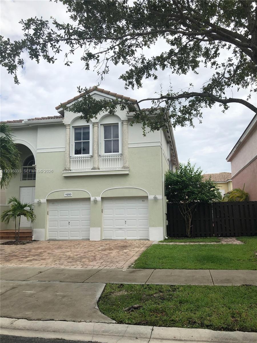 A two-story house features a light green exterior, two garage doors, and a brick driveway — 11253 NW 47th Ln, Doral FL 33178, DORAL, FL