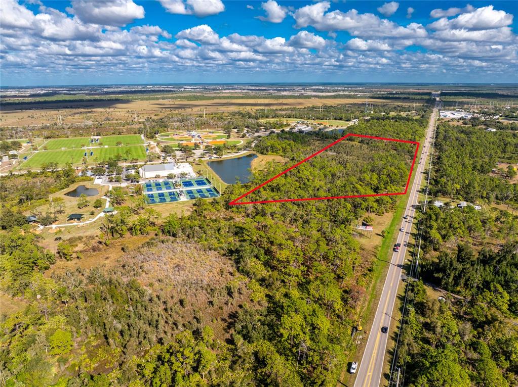 An aerial view shows a wooded lot outlined in red next to a sports complex — 0 RIVER ROAD, ENGLEWOOD, FL