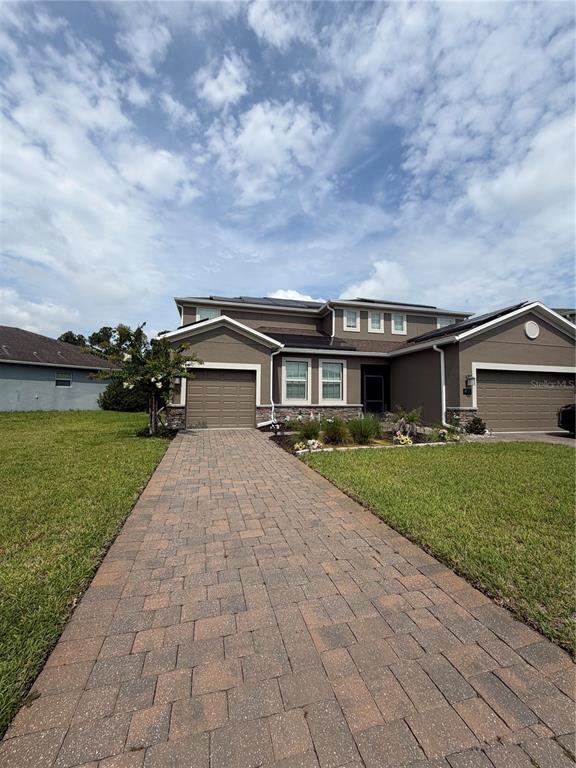 A two-story suburban house with a beige stucco exterior, solar panels, and a paved driveway — 491 BRUNSWICK DRIVE, DAVENPORT, FL