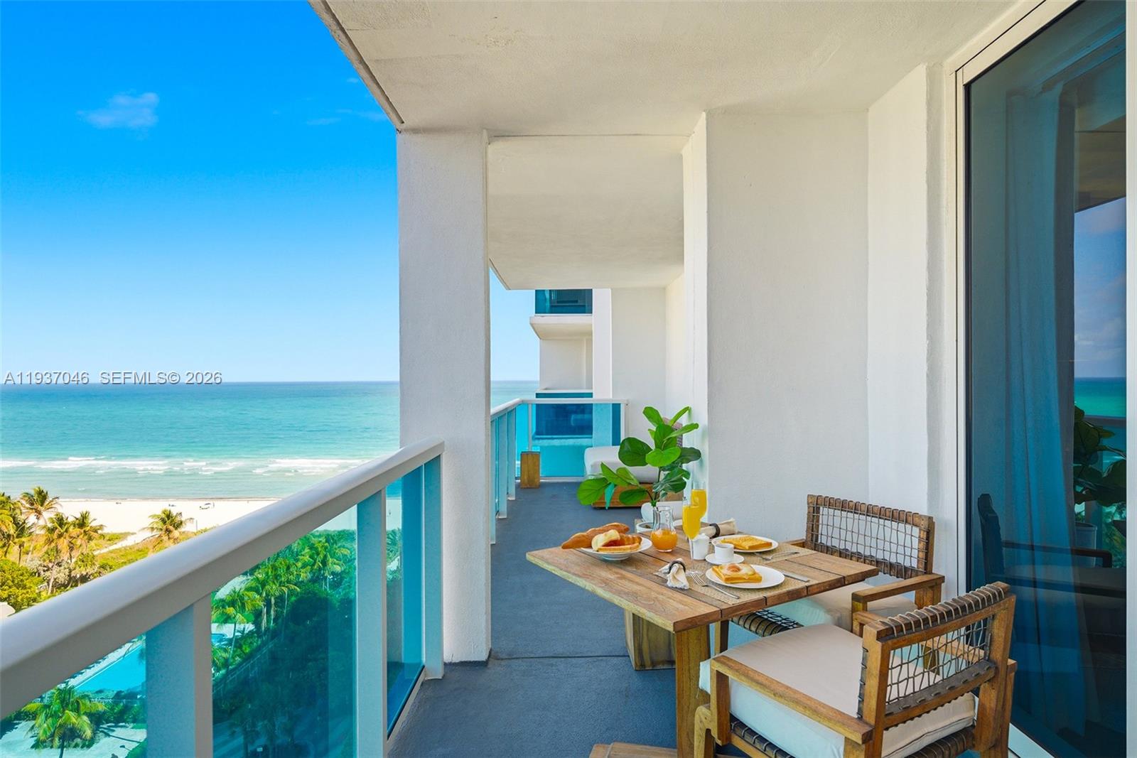 A balcony with a wooden dining set overlooks the ocean and beach below — 102 24th St # 1207, Miami Beach FL 33139, MIAMI BEACH, FL