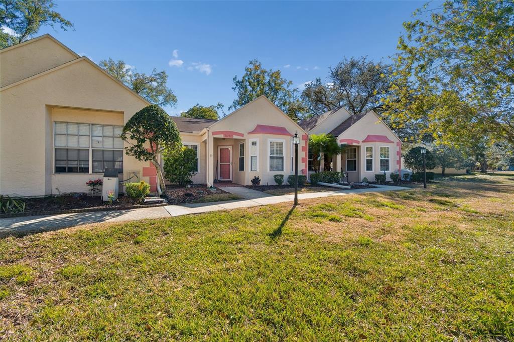 A single-story building with a light-colored stucco exterior, pink trim, and a sidewalk entrance — 11317 VERSAILLES LANE UNIT 5, PORT RICHEY, FL