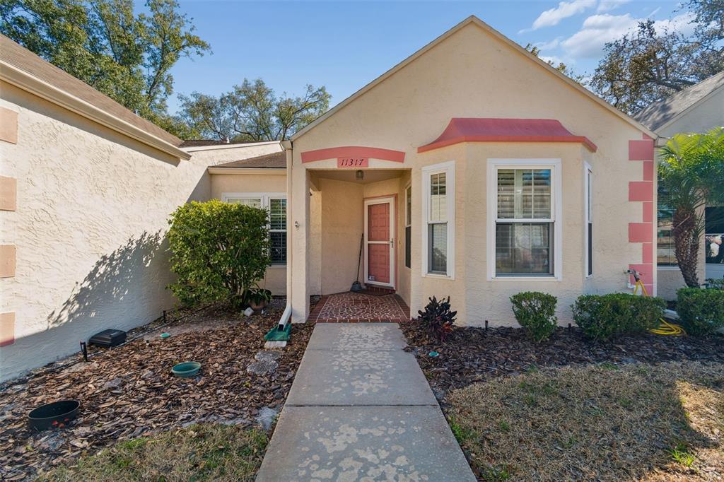 A single-story house exterior features beige stucco walls, pink trim, and a concrete walkway — 11317 VERSAILLES LANE UNIT 5, PORT RICHEY, FL