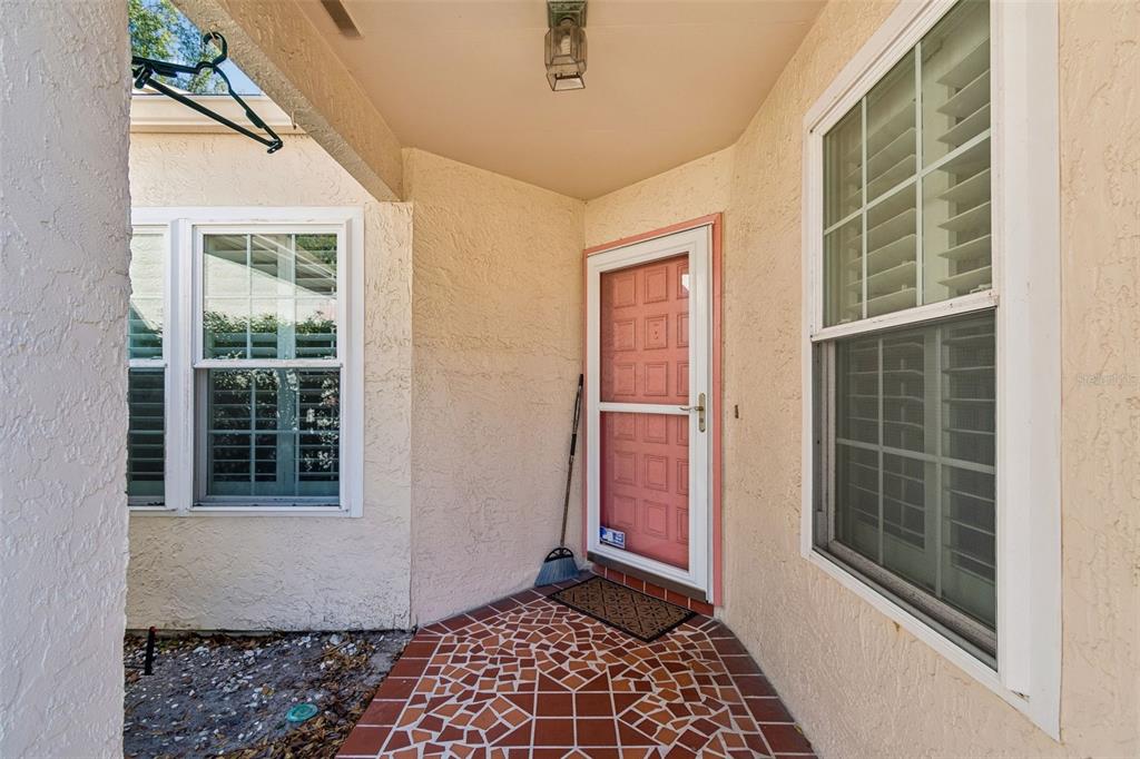 A covered entryway features a pink front door, tiled flooring, and two windows with shutters — 11317 VERSAILLES LANE UNIT 5, PORT RICHEY, FL