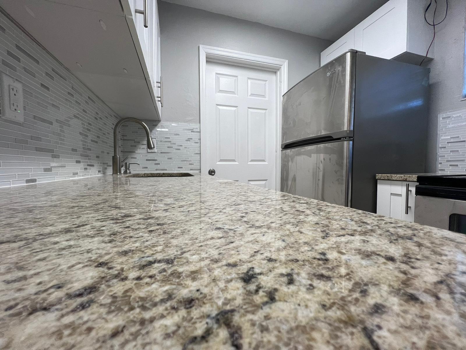 A kitchen features granite countertops, a tiled backsplash, white cabinets, and a stainless steel refrigerator — 3265 E Palm Drive, Boynton Beach FL 33435, BOYNTON BEACH, FL