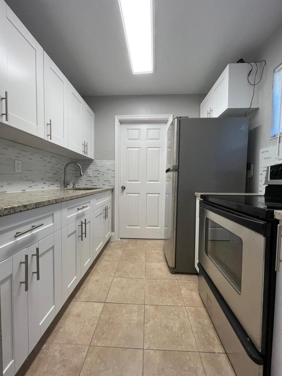 A narrow kitchen features white cabinets, stainless steel appliances, granite countertops, and tiled flooring — 3265 E Palm Drive, Boynton Beach FL 33435, BOYNTON BEACH, FL