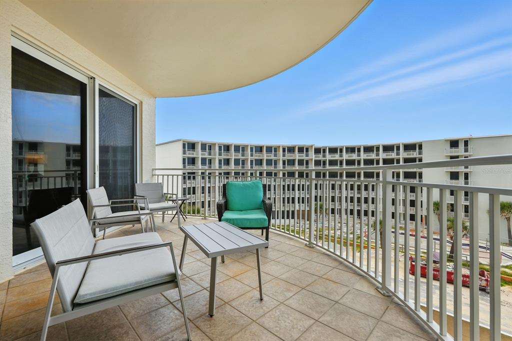 A balcony with tiled flooring, patio furniture, and a view of a large apartment complex — 2403 S ATLANTIC AVENUE UNIT 409, DAYTONA BEACH SHORES, FL