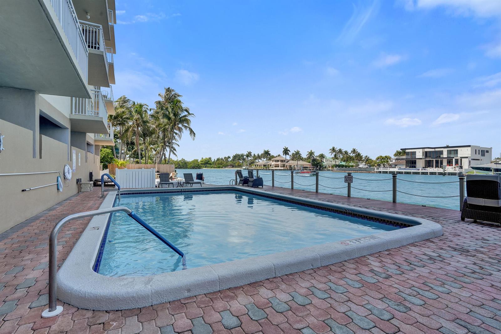 A rectangular swimming pool sits on a brick patio next to a waterfront building — 2611 N Riverside Drive # 604, Pompano Beach FL 33062, POMPANO BEACH, FL