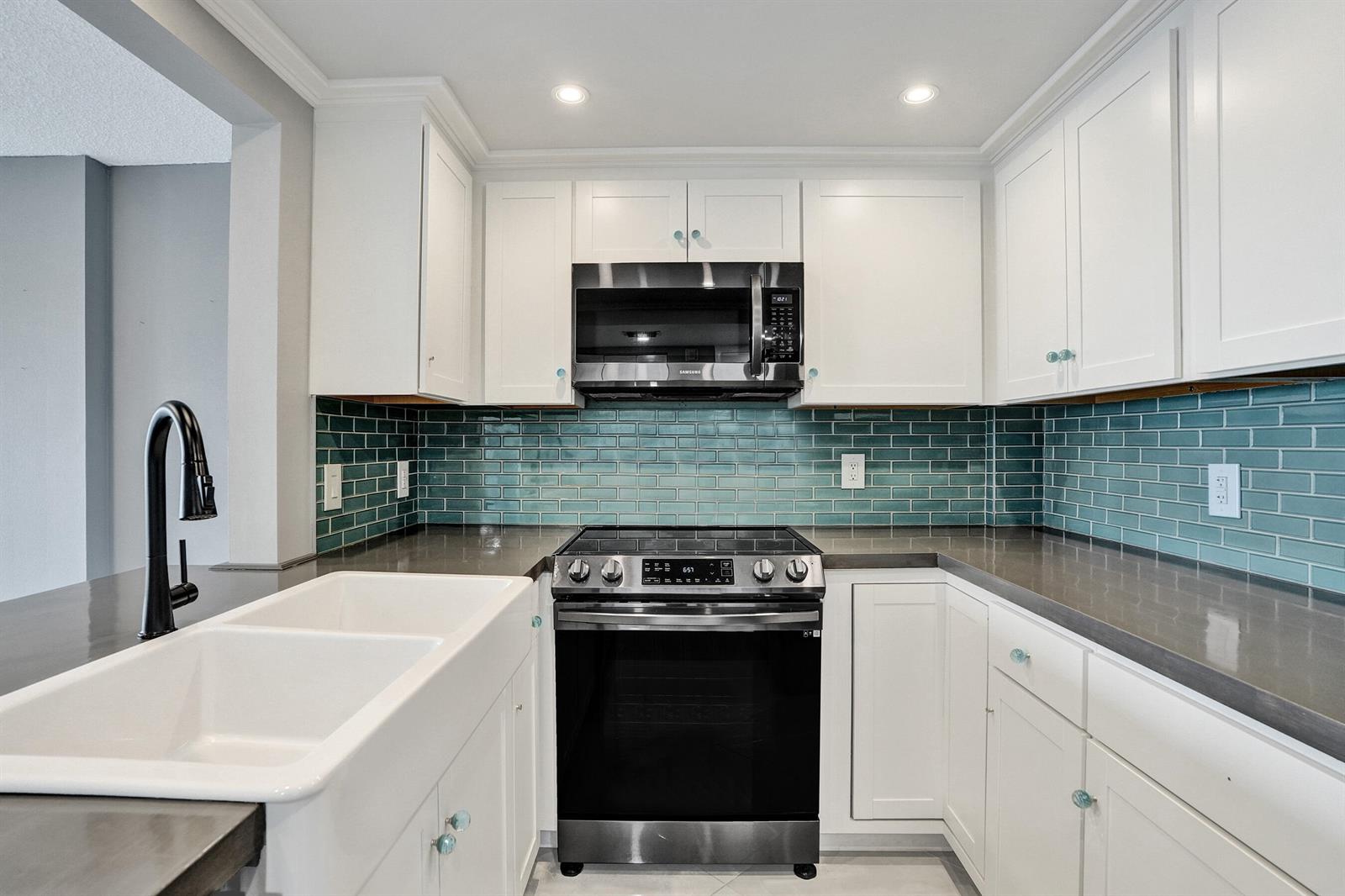 A kitchen features white cabinets, dark countertops, a teal subway tile backsplash, and stainless appliances — 2611 N Riverside Drive # 604, Pompano Beach FL 33062, POMPANO BEACH, FL