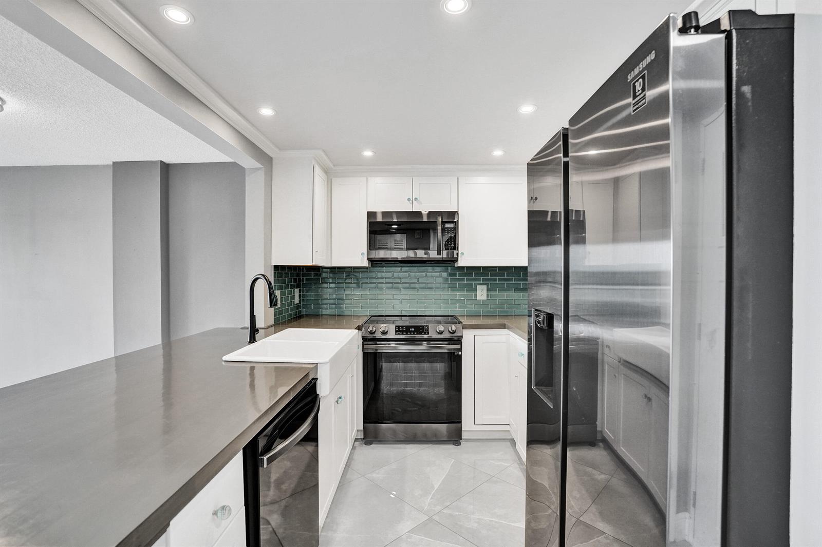 A kitchen features white cabinets, a teal subway tile backsplash, and stainless steel appliances — 2611 N Riverside Drive # 604, Pompano Beach FL 33062, POMPANO BEACH, FL