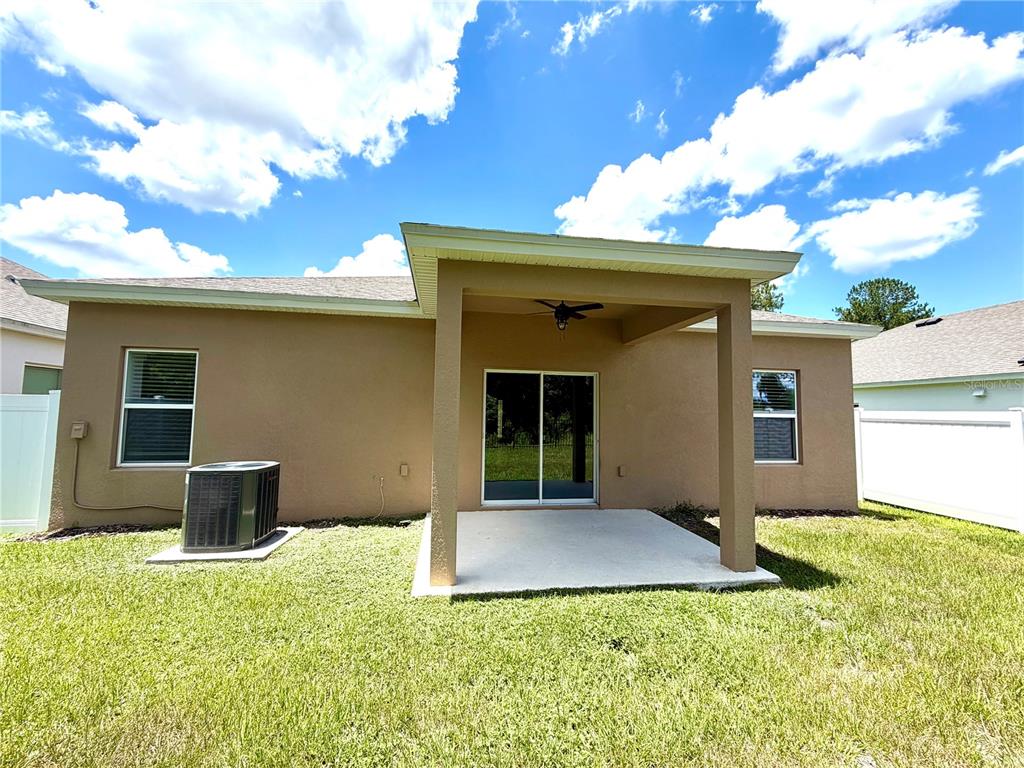 The exterior rear view of a house features a covered patio, lawn, and HVAC unit — 9136 CAPE COD ROAD, DELAND, FL
