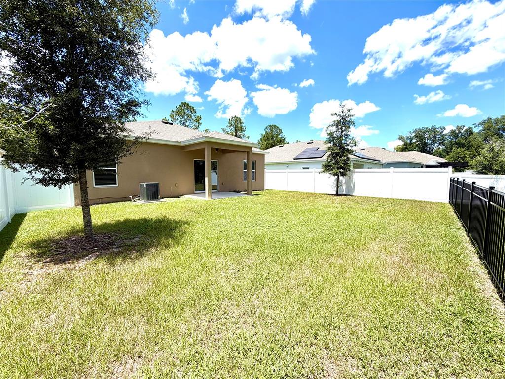 The backyard of a house features a covered patio, a lawn, and white vinyl fencing — 9136 CAPE COD ROAD, DELAND, FL