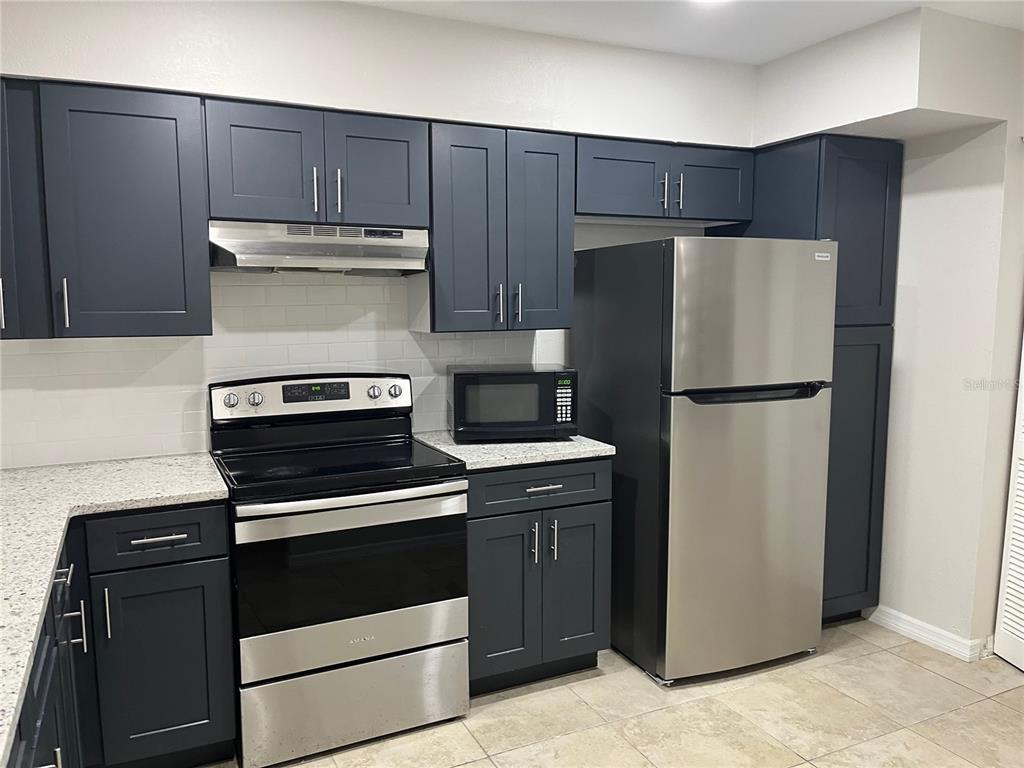 A kitchen features dark blue cabinets, stainless steel appliances, and light-colored granite countertops — 4372 MIDDLEBROOK ROAD UNIT 4372, ORLANDO, FL