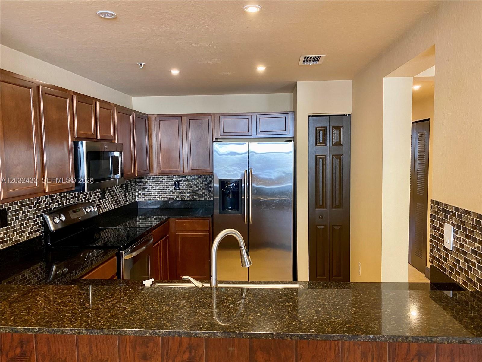 A kitchen features dark wood cabinets, granite countertops, stainless steel appliances, and a tiled backsplash — 8800 NW 107th CT # 110, Doral FL 33178, DORAL, FL